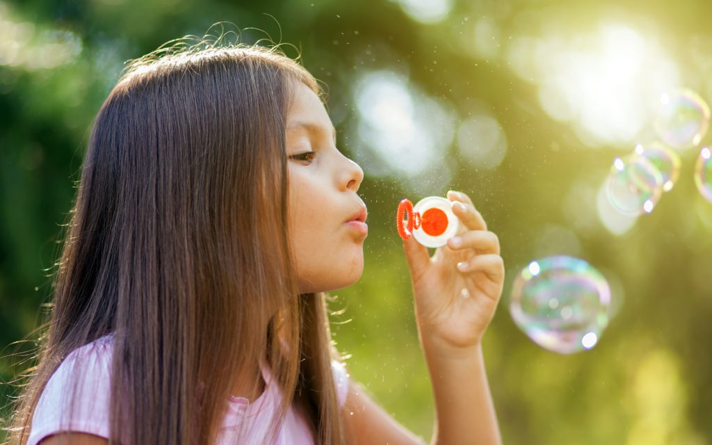 Children girl blowing soap bubbles in outdoor forest